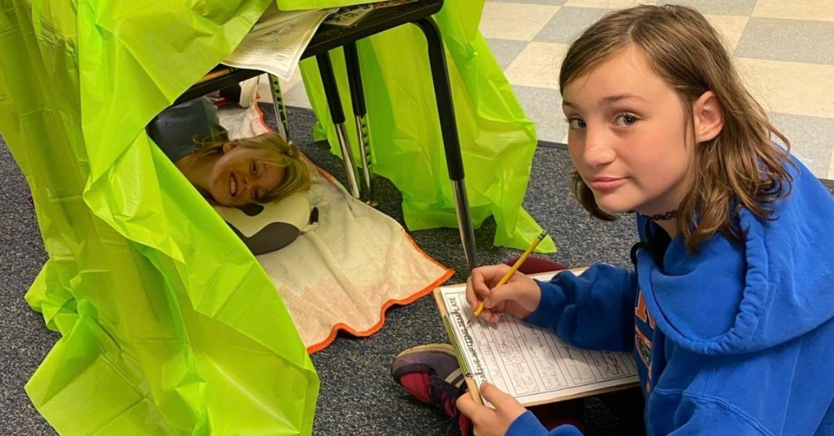 Danika Troy sits on a floor, writing on a piece of paper.