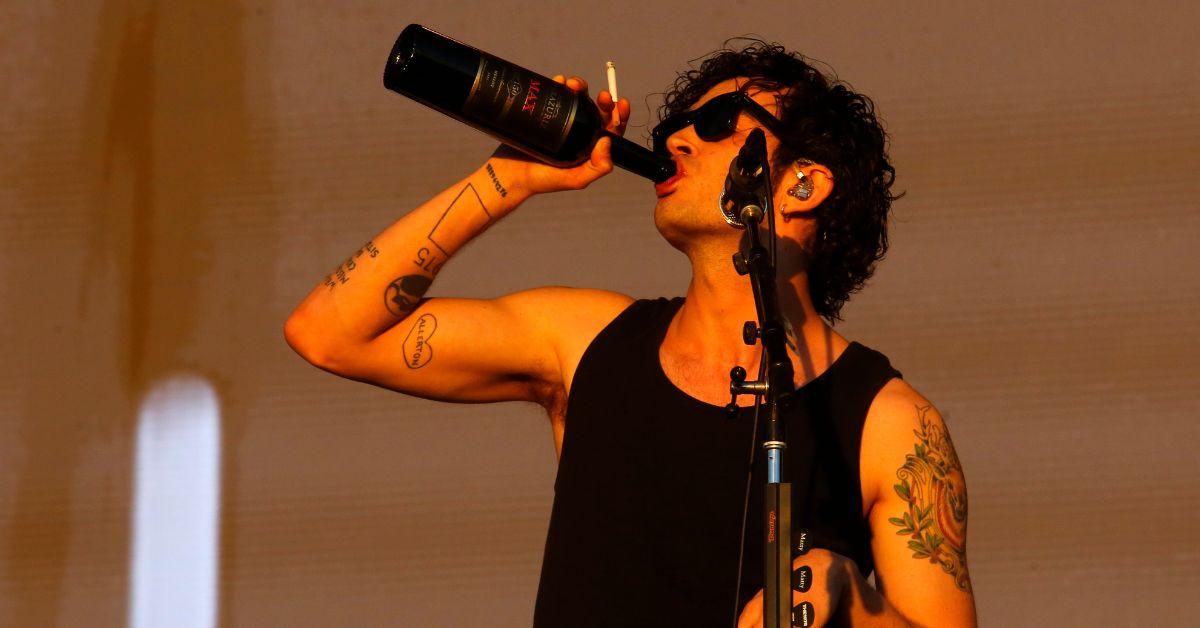 Matty Healy performs on stage at Lollapalooza Chile 2023, drinking from a bottle and smoking a cigarette
