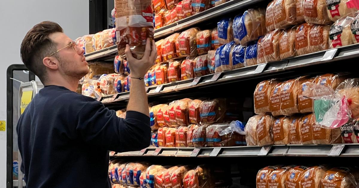 A  man picking out a loaf of bread at a grocery store