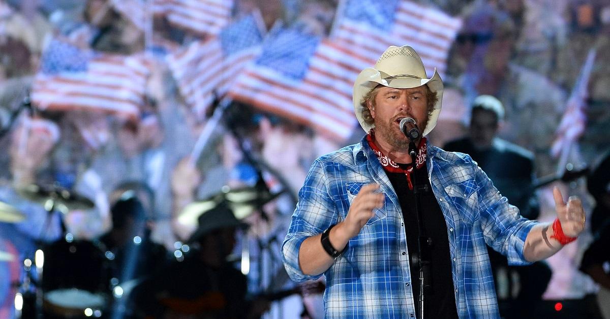 toby keith performs in blue flannel shirt, with american flags behind him