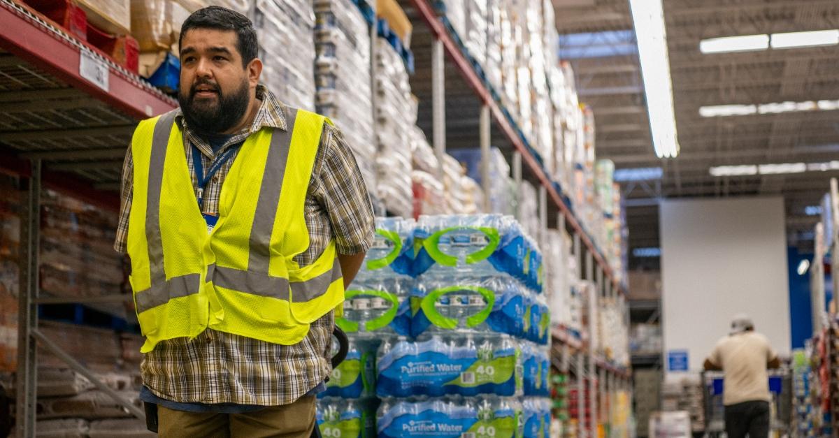 Man wears safety vest pulls a rolling cart with a stack of bottled water.