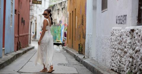 Shay Mitchell looking back over her shoulder while wearing a white matching set surrounded by colorful buildings in South America.