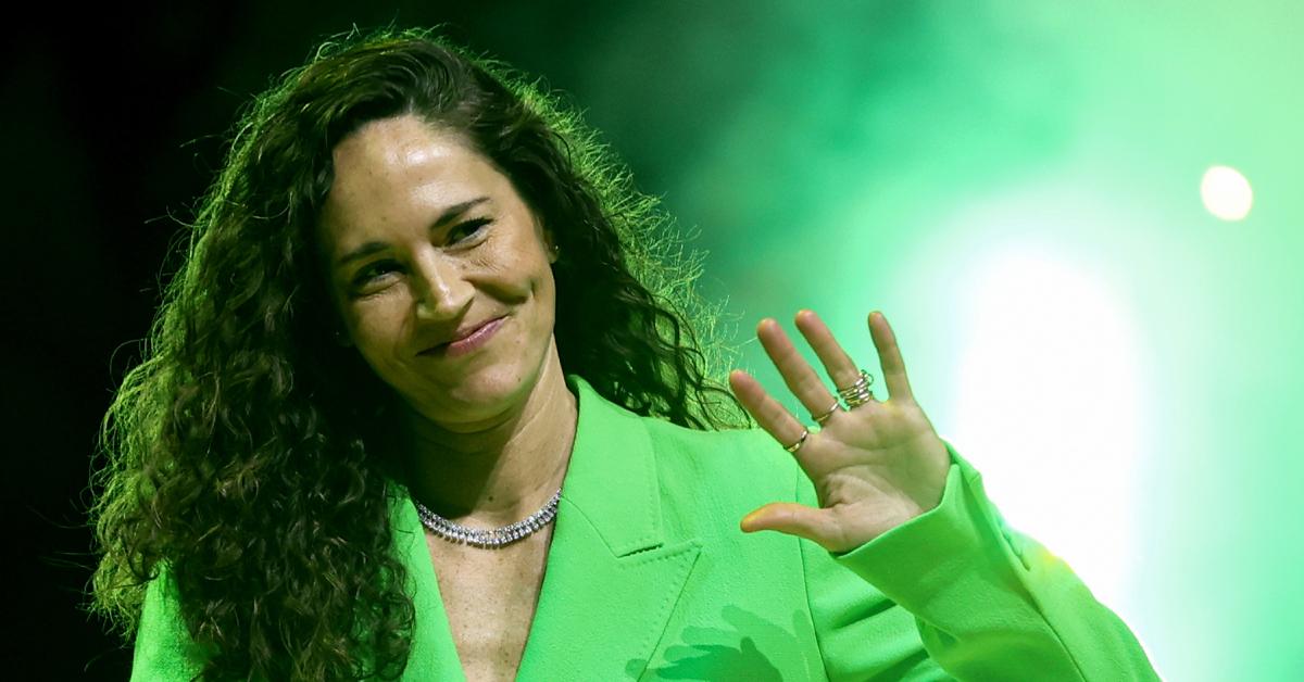 Sue Bird, sporting a bright green suit, waves to someone in the crowd during her jersey retirement ceremony on June 11, 2023.