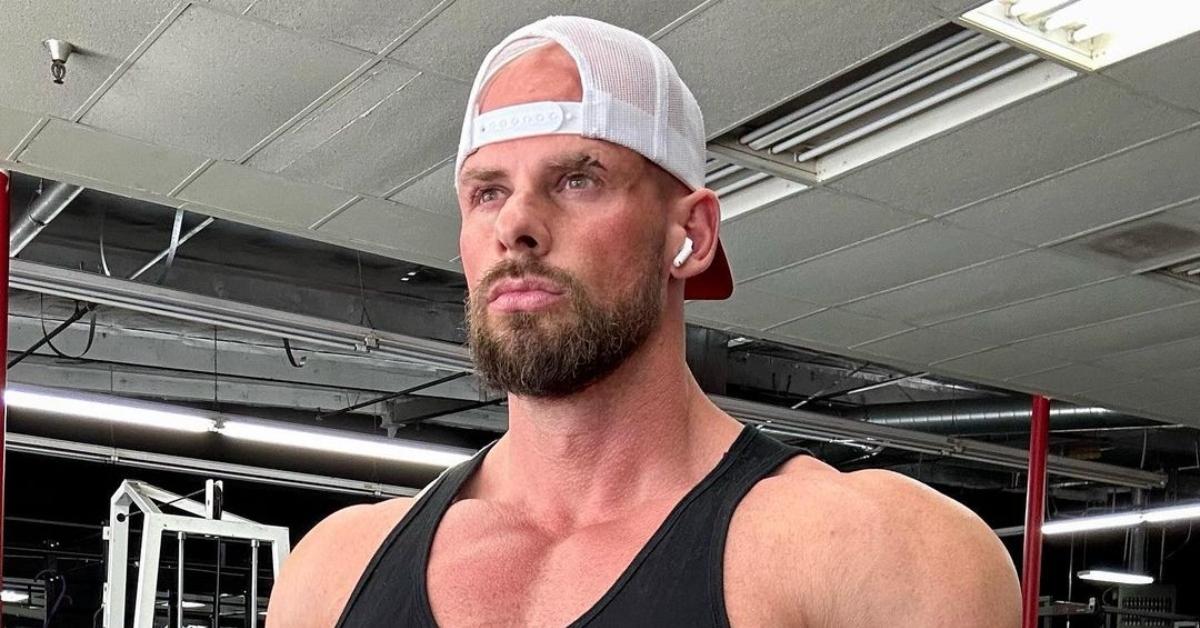 Joey Swole in a black tank top and white trucker hat looks serious at the gym.