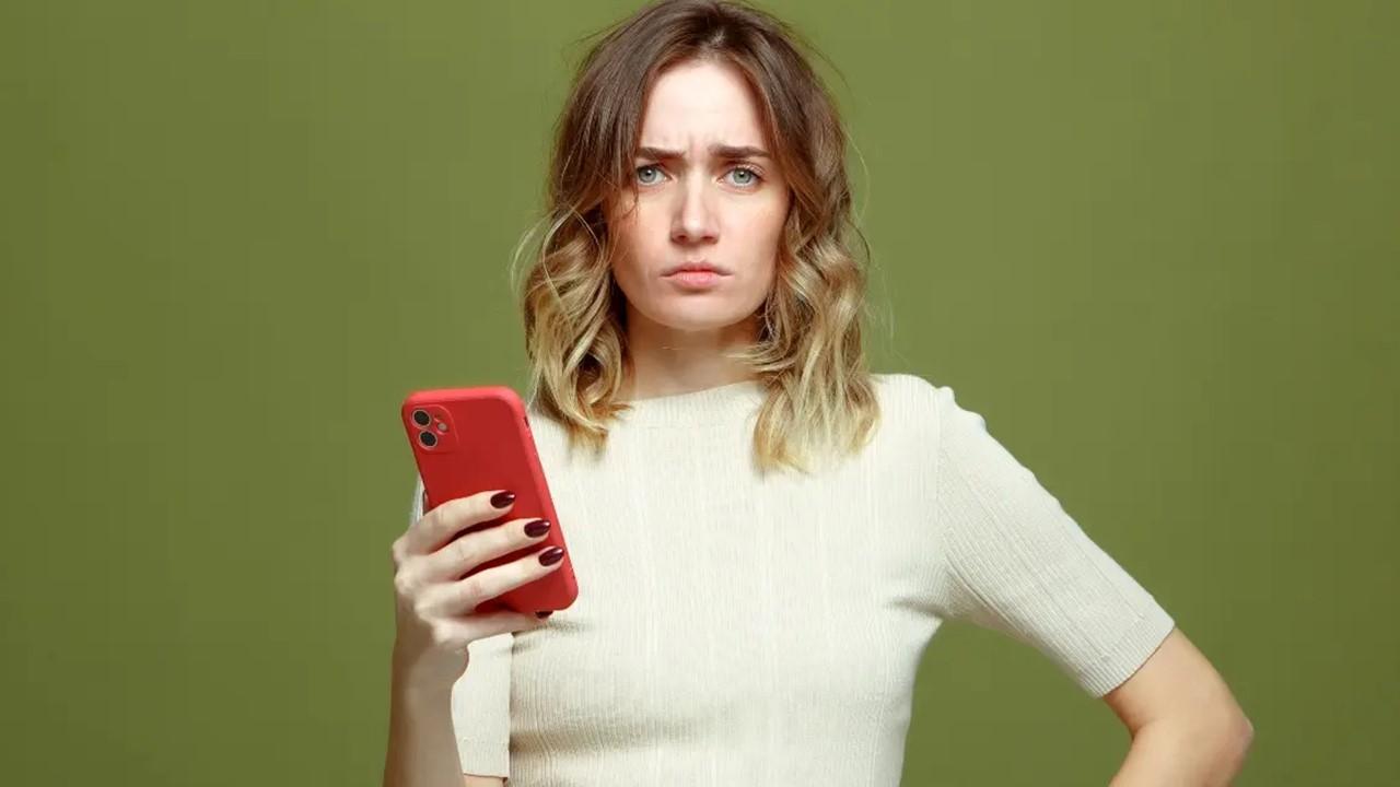 A woman holding cell phone and looking confused