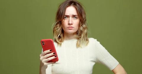 A woman holding cell phone and looking confused