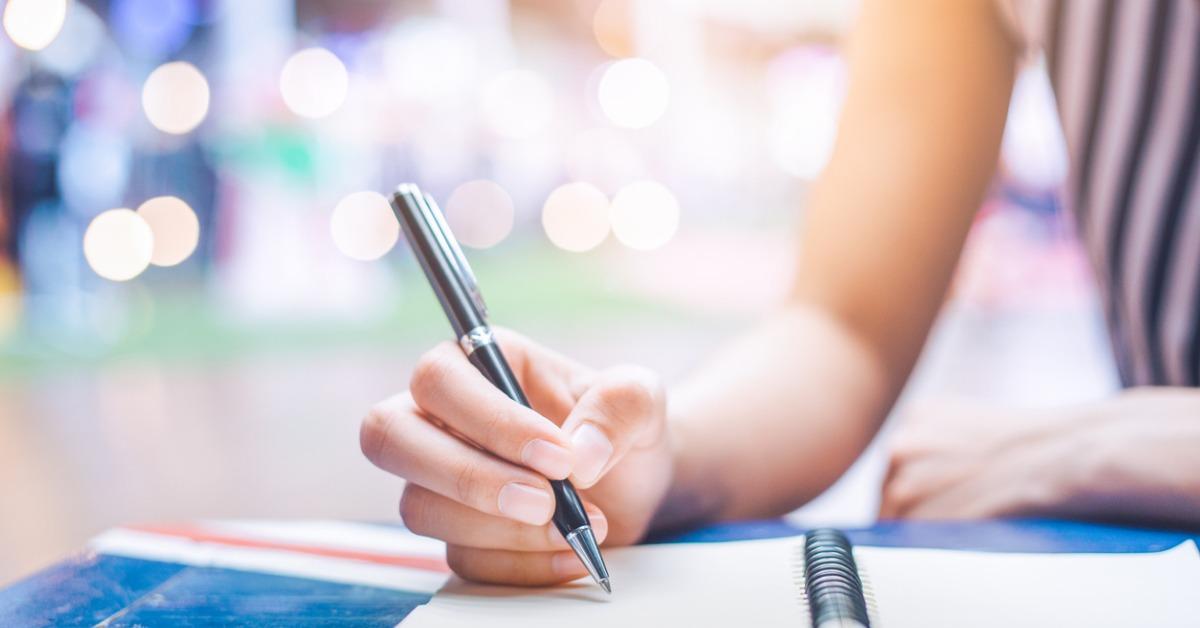 womans hand writing on a notebook with a pen on a wooden desk picture id