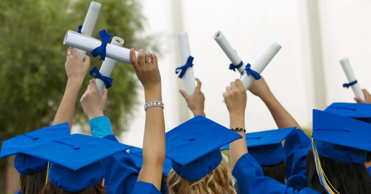 grads in caps and gowns hold up their diplomas