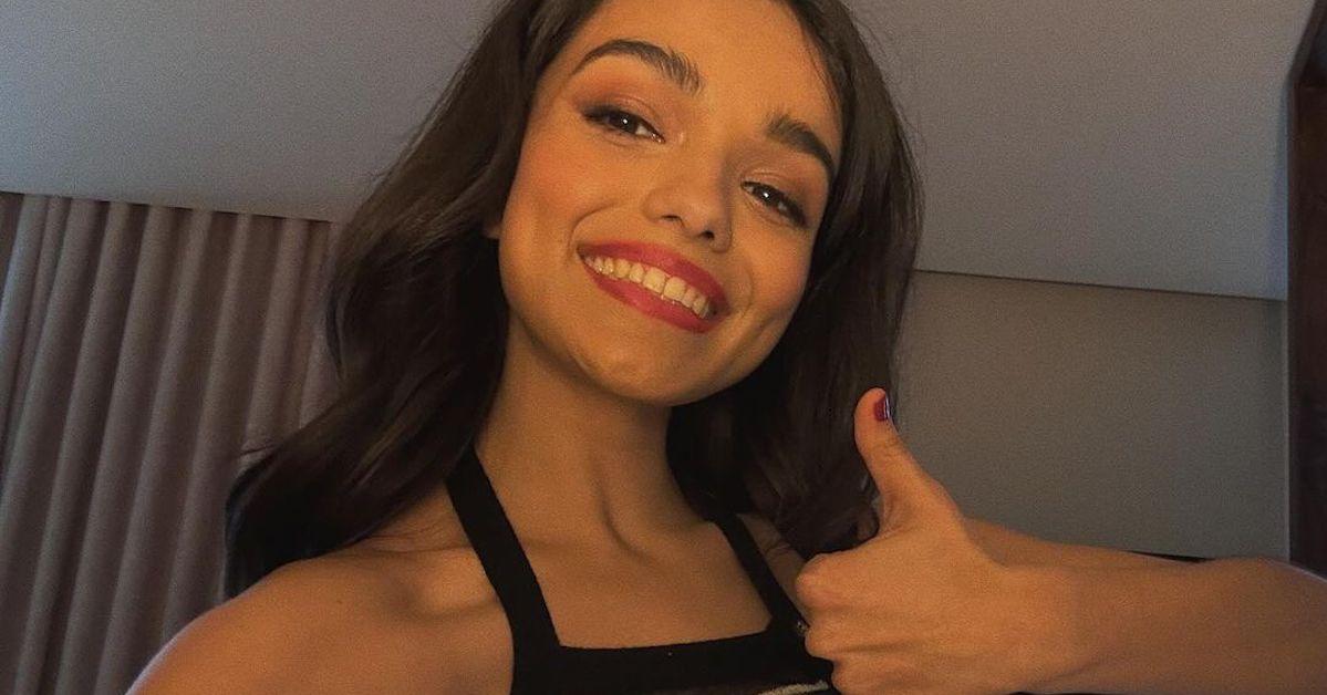 Rachel Zegler smiles wearing red lipstick and giving a thumbs up