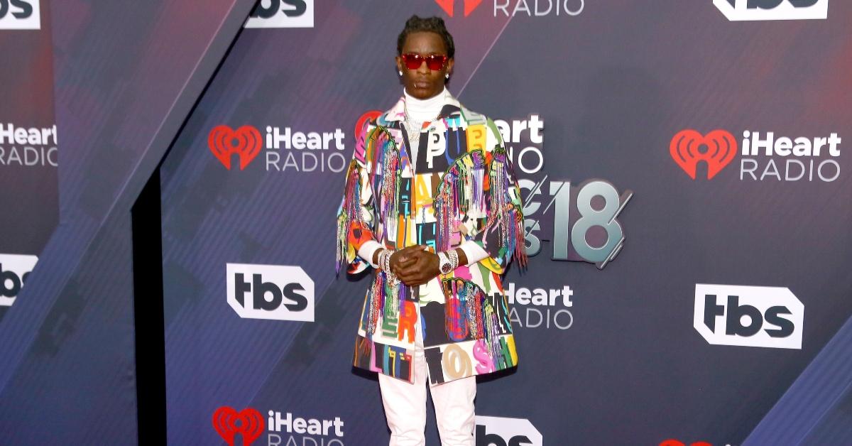 Young Thug posing in a colorful jacket and sunglasses at the 2018 iHeartRadio Music Awards. 