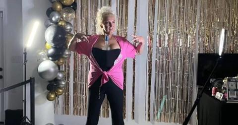 Angela Deem wears a black jumpsuit and pink sweater.