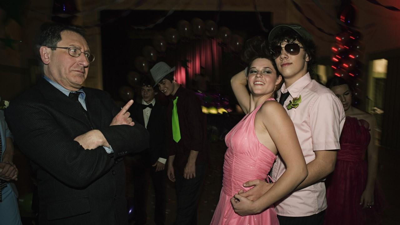 A couple dancing at prom with a teacher watching