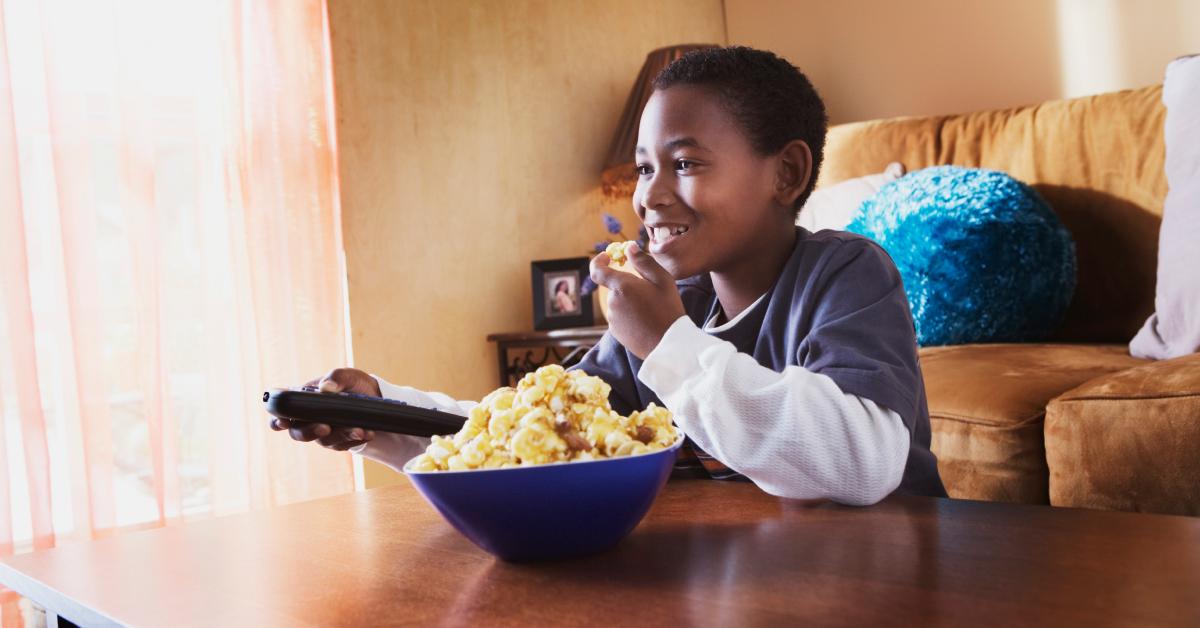 A boy eating popcorn and watching a movie in his living room.