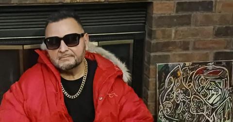 Charlie Rock LD sitting by a fireplace in a red jacket, black shirt, and sunglasses