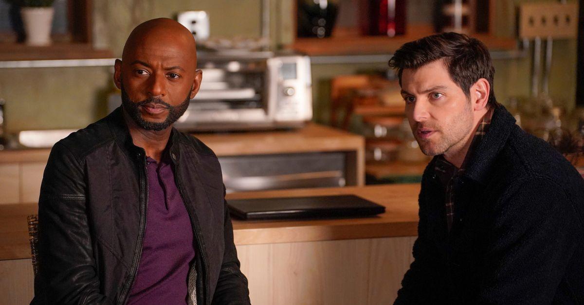 (l-r): Romany Malco as Rome and David Giuntoli as Eddie looking away while sitting in Gary's living room.