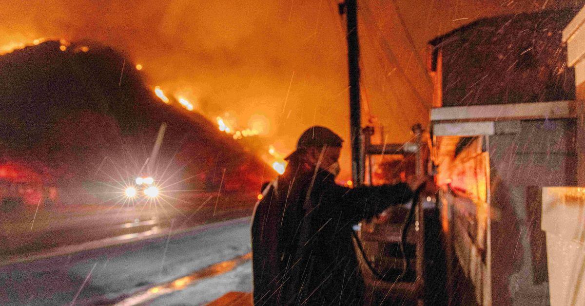 A man standing in front of a hillside on fire. 