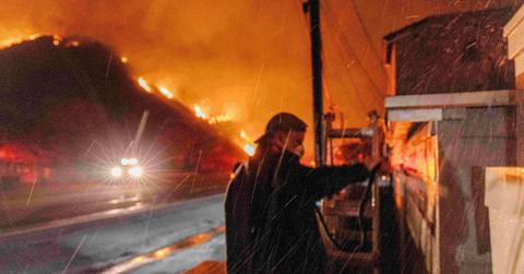 A man standing in front of a hillside on fire.