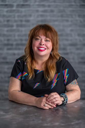 Deanna wears a black shirt adorned with rainbow lightning strikes, smiling for her official portrait for Season 2 of 'The Mole.'