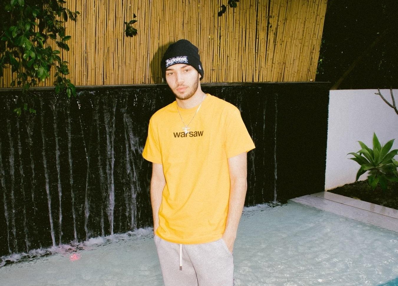 Adin Ross posing next to a pool in a yellow t-shirt.