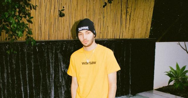 Adin Ross posing next to a pool in a yellow t-shirt.