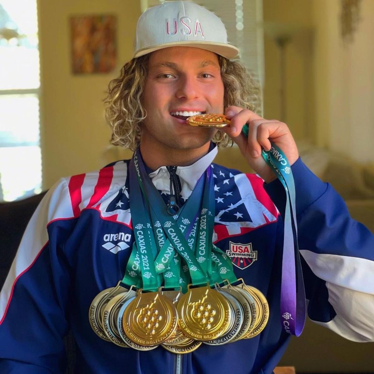 'Big Brother 25' star Matt Klotz wears red, white, and blue tracksuit and deaflympic medals around his neck, bites down on gold medal.