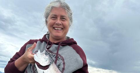 Sue Aikens holding a fish and wearing a hoodie.