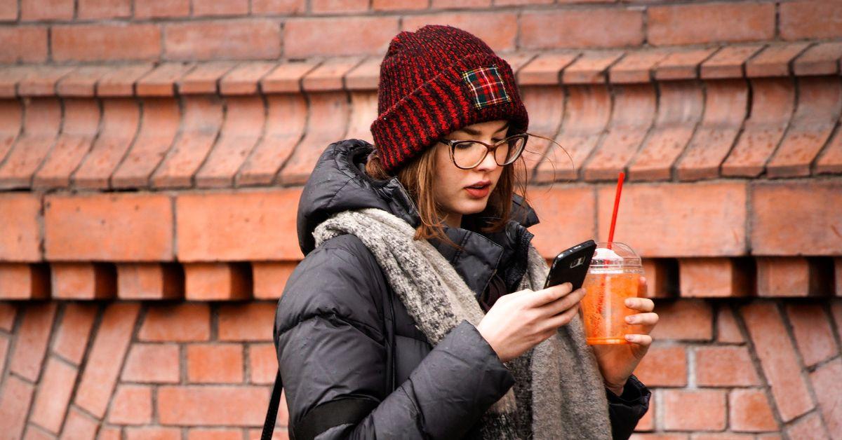 A woman reading her phone while holding a drink in her other hand