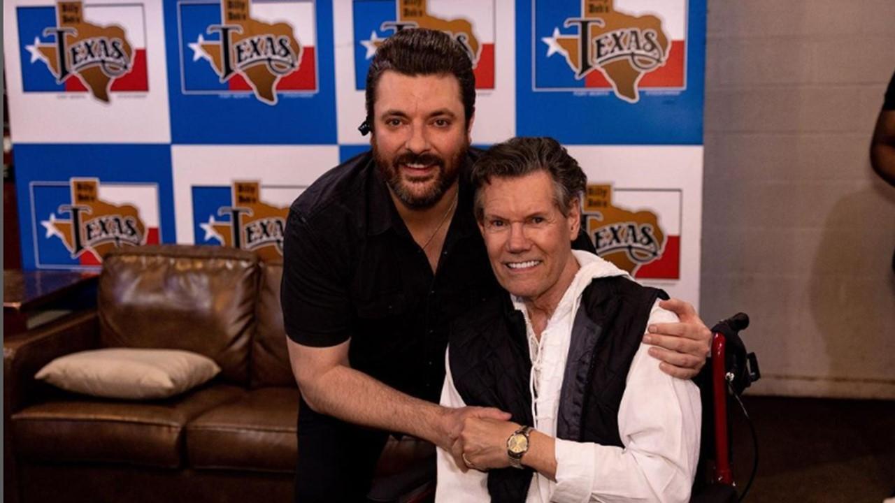 Randy Travis sitting in a wheelchair and holding Chris Young's hand