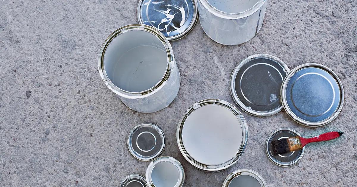 A series of paint cans that are open and sitting on concrete. 