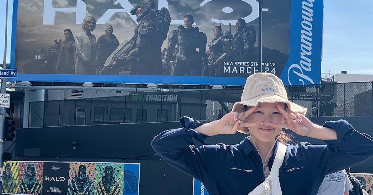 Yerin Ha stands in front of a billboard for 'Halo' in L.A. in 2022 wearing a bucket hat and blue jacket