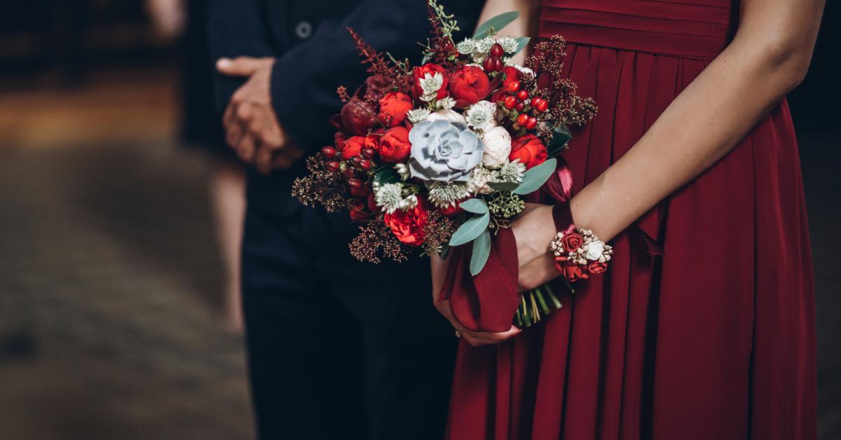 A bridesmaid wears a red gown while holding a rustic bouquet.