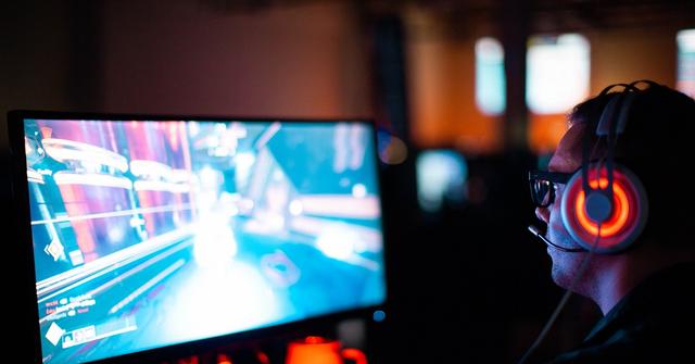 Gamer with red headphones planning a shooting game on a PC screen.