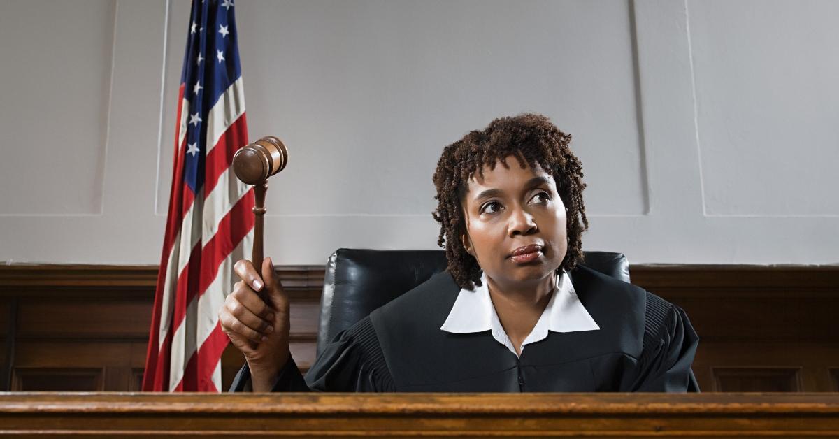 Black female judge with short locs bangs gavel in courtroom.