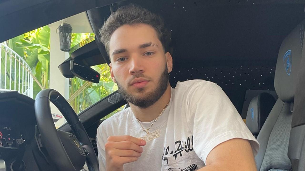 Adin Ross wearing a white t-shirt and boss necklace in a car