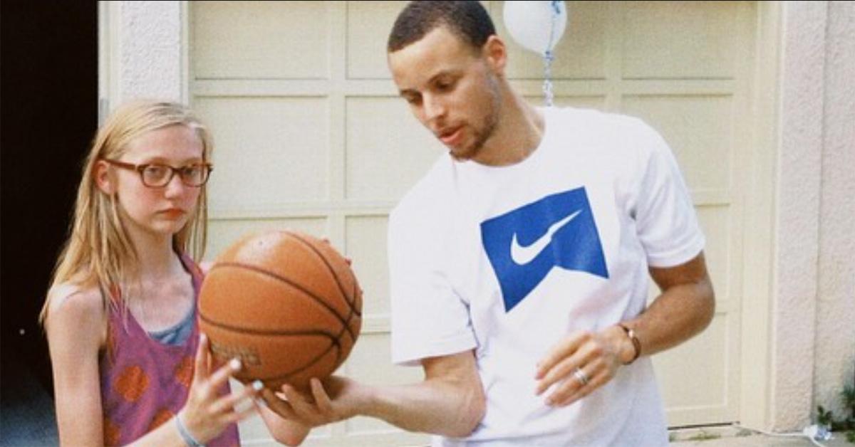 Steph Curry holding a basketball with a young Cameron Brink. 