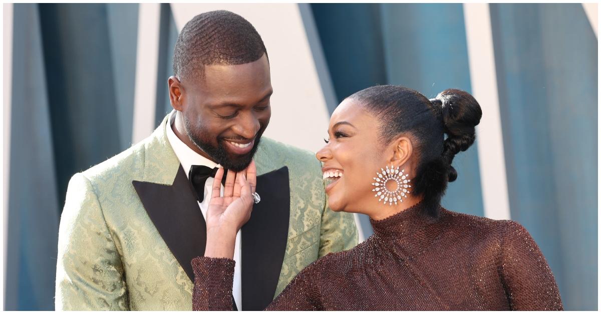 (l-r): Dwyane Wade smiling while looking down at his wife, Gabrielle Union, who is wearing a sequined turtleneck dress and silver earrings.