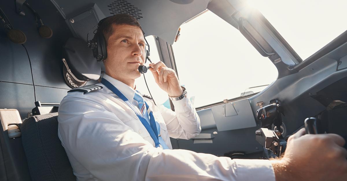 A pilot sits in the cockpit of an airplane with a headset on