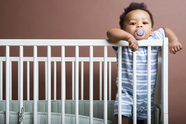 Baby in blue standing in white cot