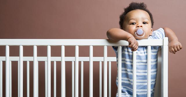 Baby in blue standing in white cot
