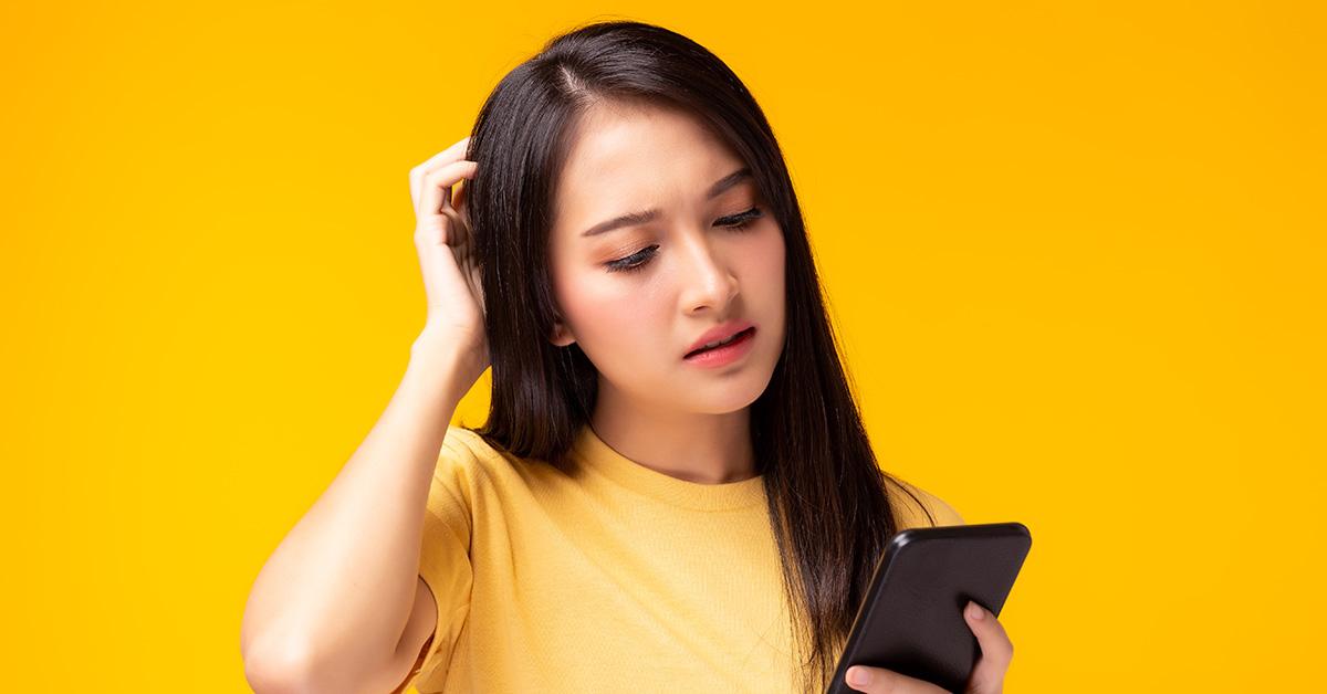 A woman looking at a phone and scratching her head. 