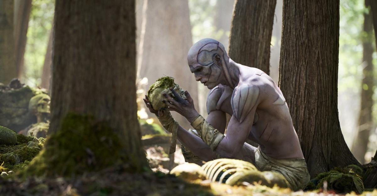 The Creature looking at a crushed skull in the forest in Frankenstein