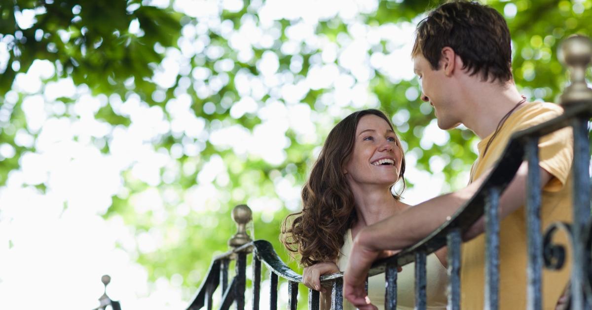 man and woman smile and flirt with each other outside by bridge