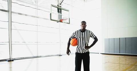 A referee on a basketball court holding a basketball.