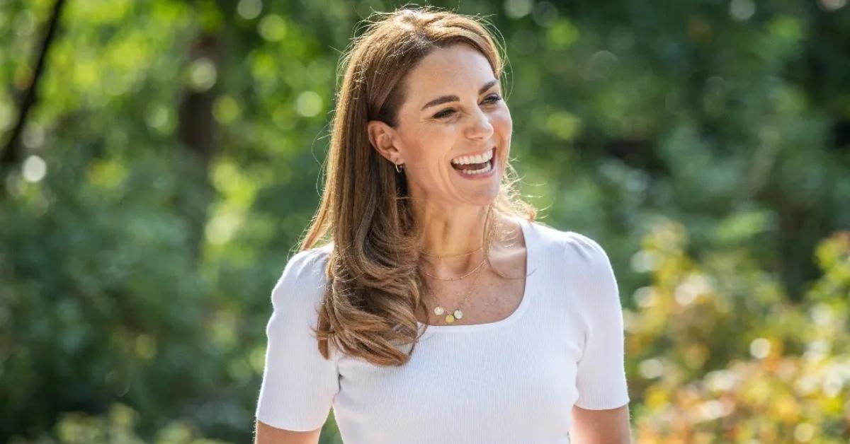 Kate Middleton wearing a white top and smiling while outdoors.