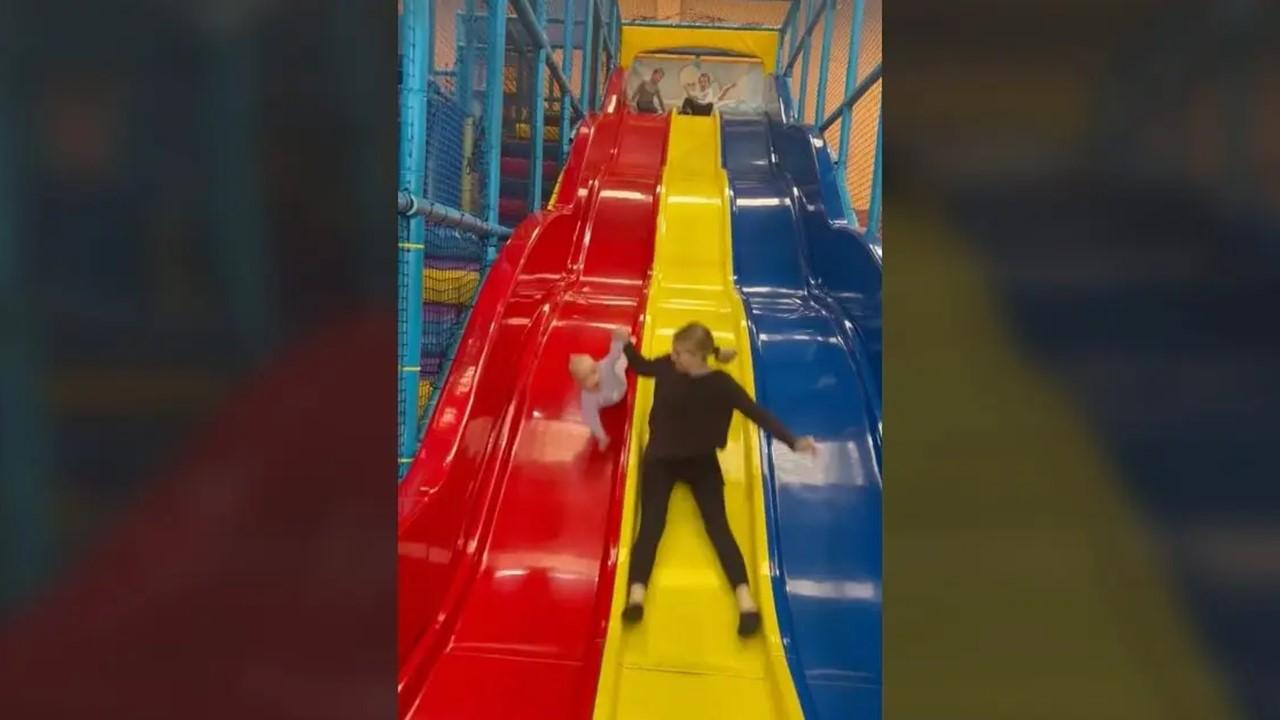 The mom is losing control of the baby as they go down the slides