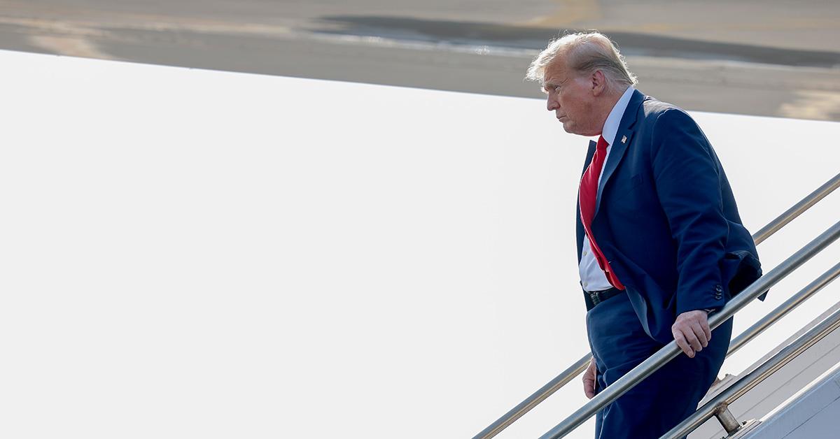 Donald Trump exiting a plane in a suit and tie. 