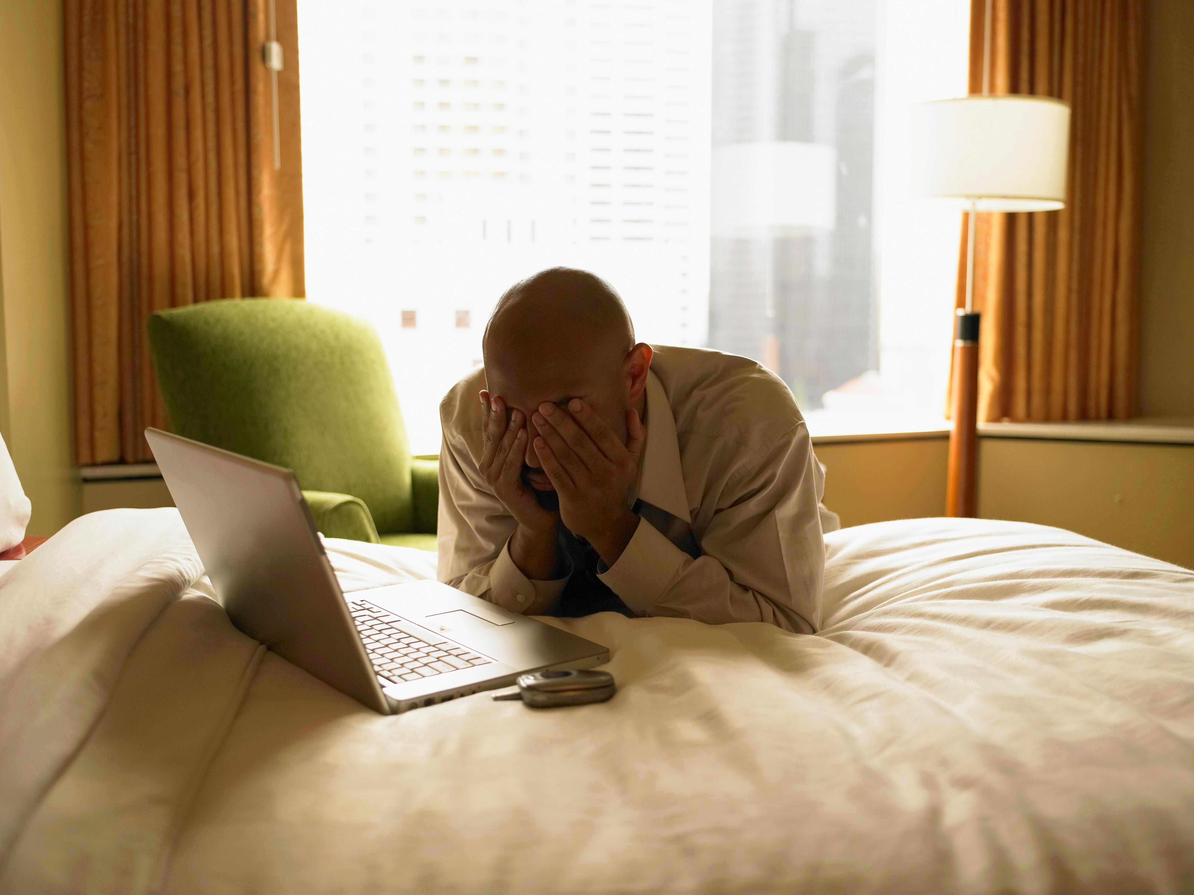 A man looks exhausted and stressed while working from a hotel.