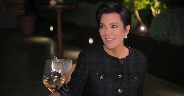 Kris Jenner, wearing an all-white ensemble, smiles and holds out her wine glass in Season 5 of 'The Kardashians.'