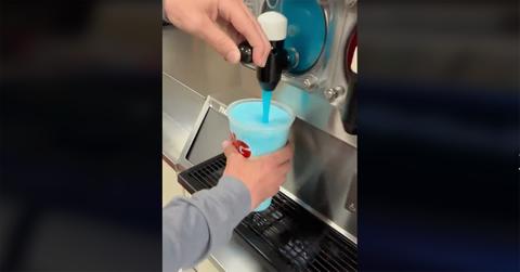 A hand holding a blue slushie over a dispenser.