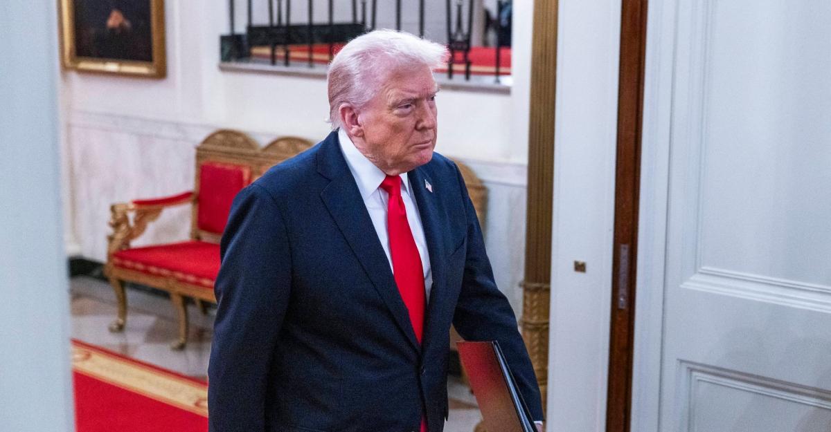 Trump walks through the White House wearing a red tie and a U.S. flag pin.